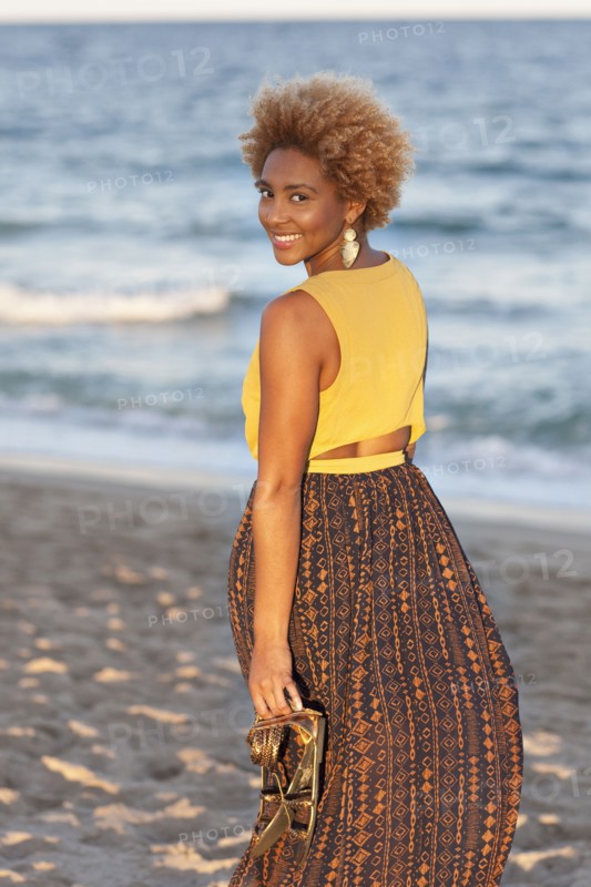 Black woman carrying sandals on beach