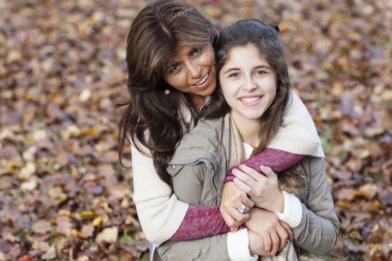 Hispanic mother and daughter hugging in autumn leaves