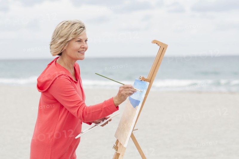 Older Caucasian woman painting on beach