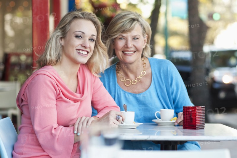 Caucasian mother and daughter drinking coffee at sidewalk cafe