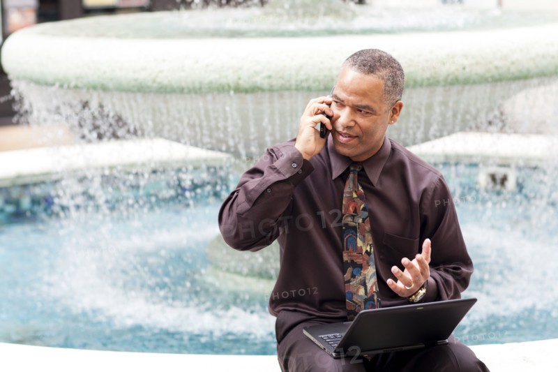 African American businessman talking on cell phone at fountain