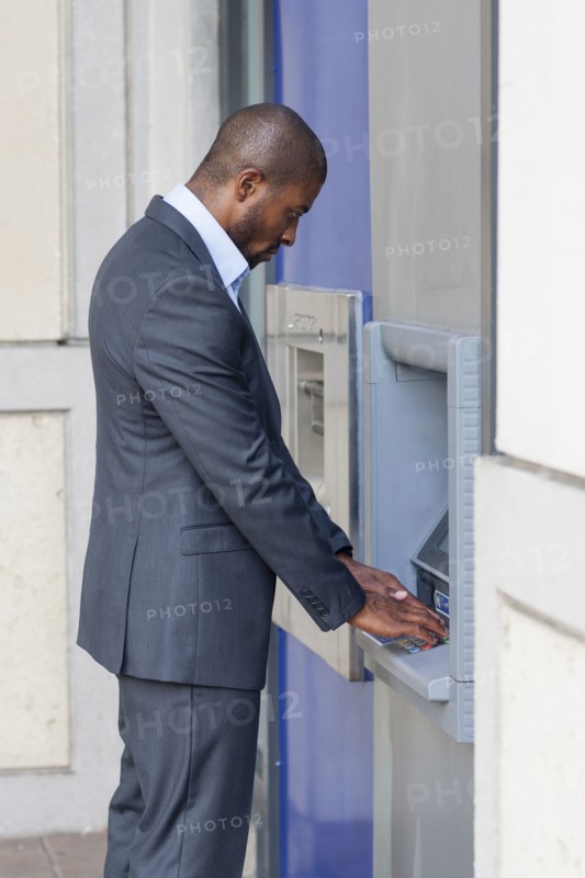 Black businessman using ATM in city