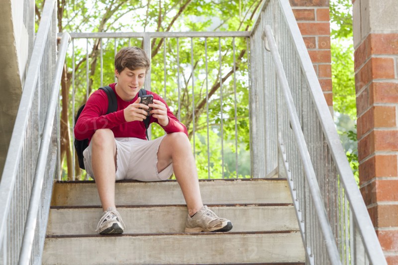Caucasian teenage boy using cell phone on steps