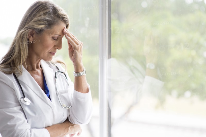 Caucasian doctor rubbing forehead at window