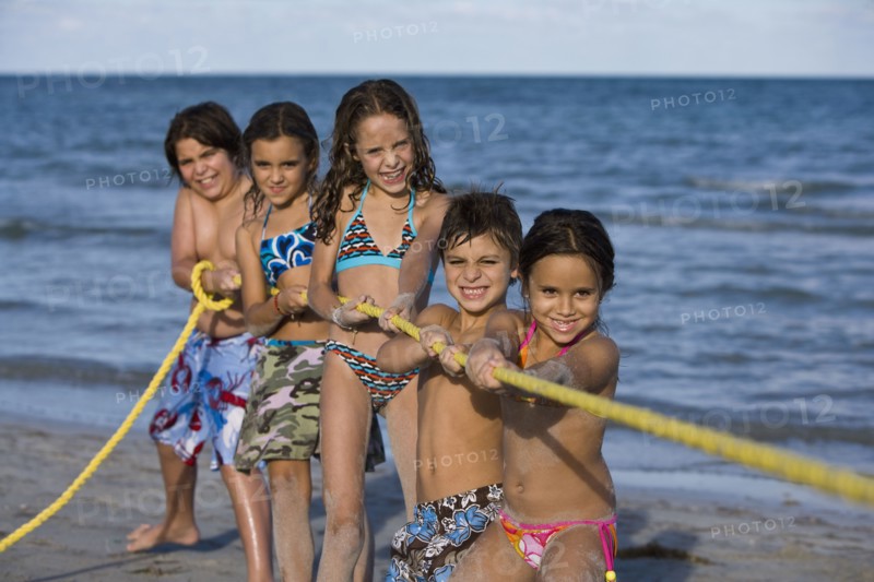 Hispanic children playing tug-of-war on beach