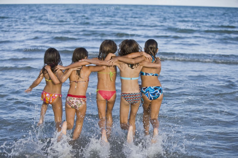 Hispanic girls running through ocean surf