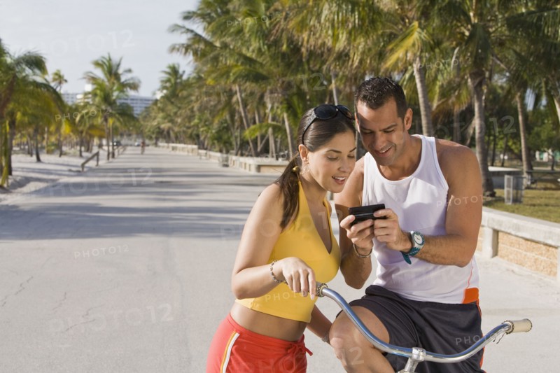 Hispanic couple on bicycles looking at cell phone
