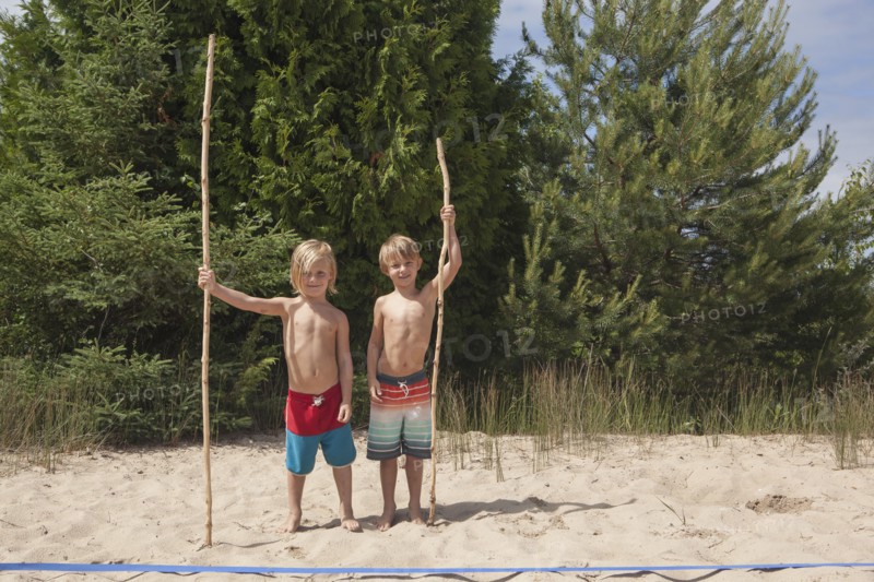 Caucasian boys holding sticks on beach