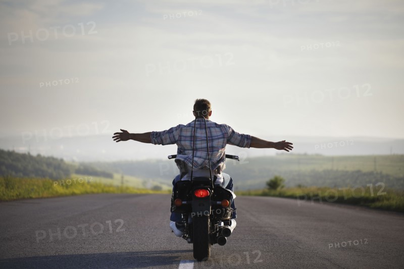 Caucasian man riding motorcycle with arms outstretched