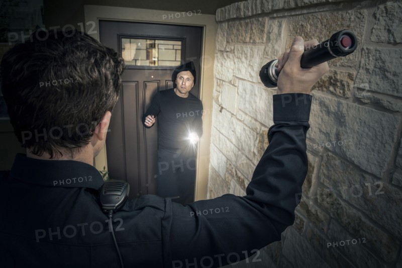 Caucasian police officer shining flashlight on house burglar