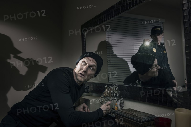 Caucasian police officer shining flashlight on house burglar