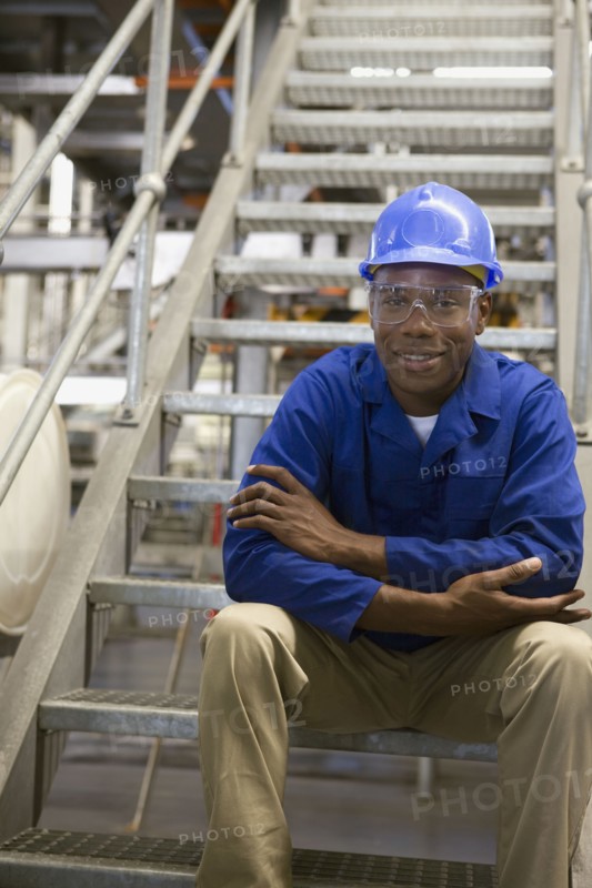 African worker in hard-hat sitting on metal staircase