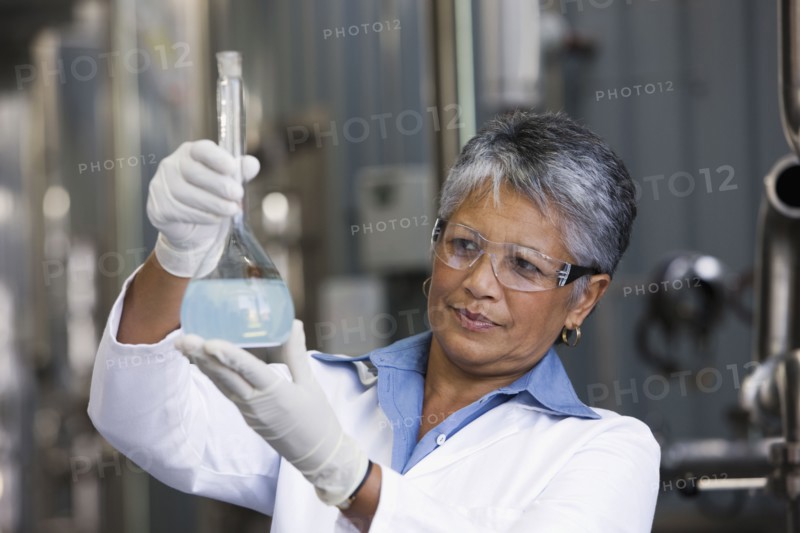 African scientist examining beaker of liquid in factory
