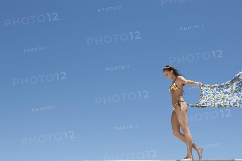 Caucasian woman in bikini holding sarong in wind