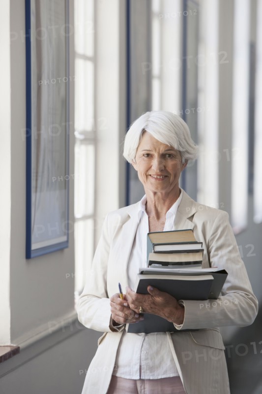Senior Caucasian businesswoman carrying books in office