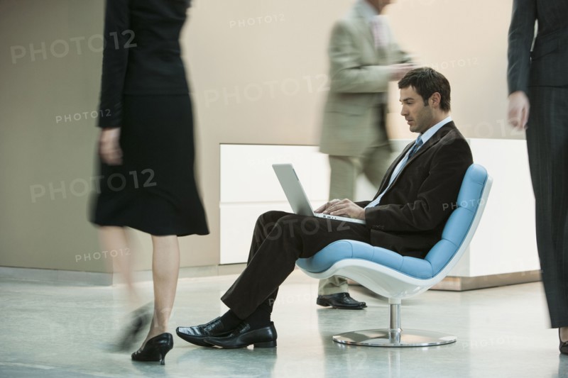 Businessman working on laptop in busy lobby area