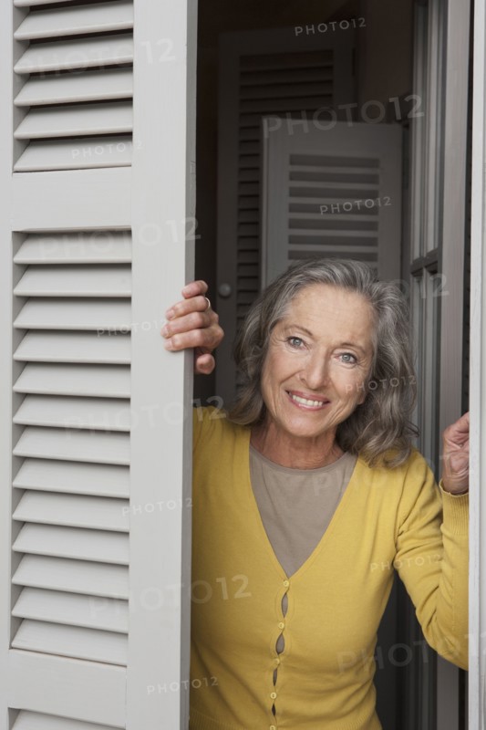 Woman peering out window shutters