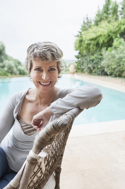 Woman smiling in armchair by swimming pool