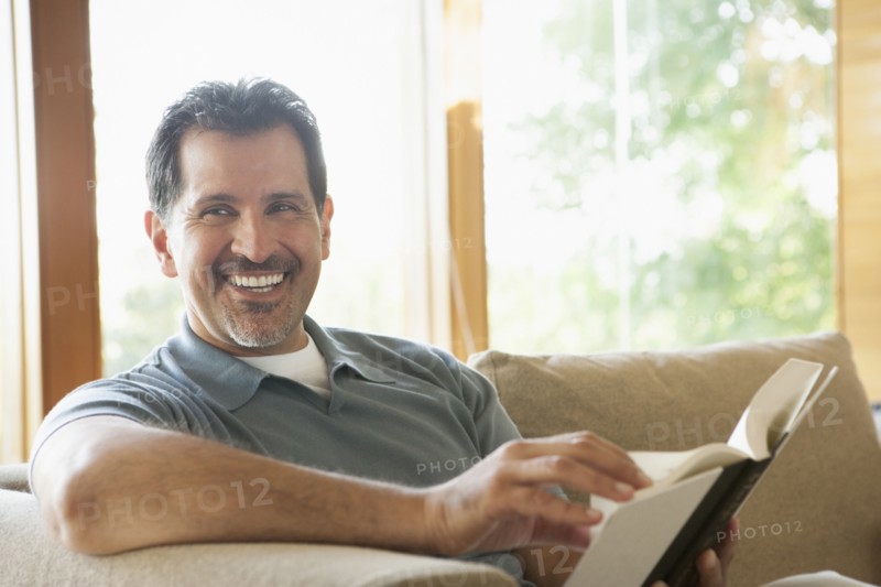 Hispanic man reading on sofa