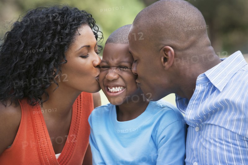 African American parents kissing son's cheeks