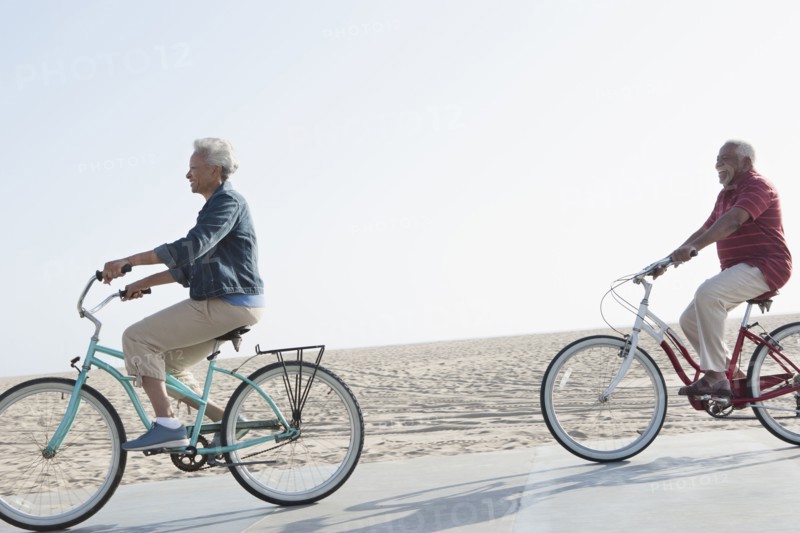 Senior African American couple riding bicycles by beach