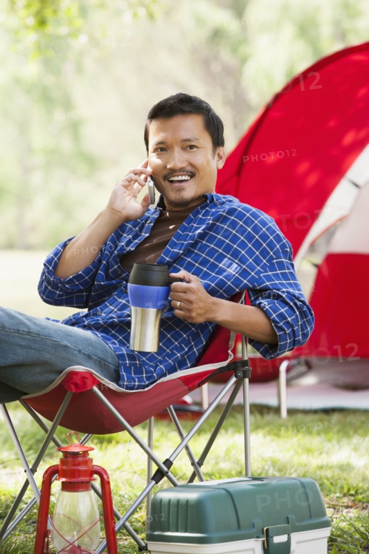 Asian man relaxing in lawn chair at campsite