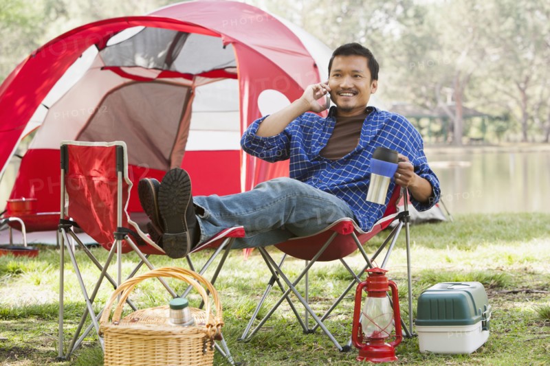 Asian man relaxing in lawn chair at campsite