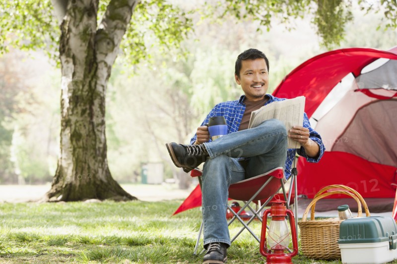 Asian man relaxing in lawn chair at campsite