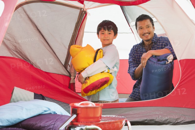 Asian father and son unpacking in tent