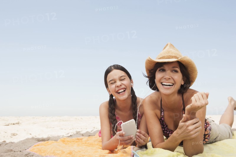 Mother and daughter listening to headphones on beach