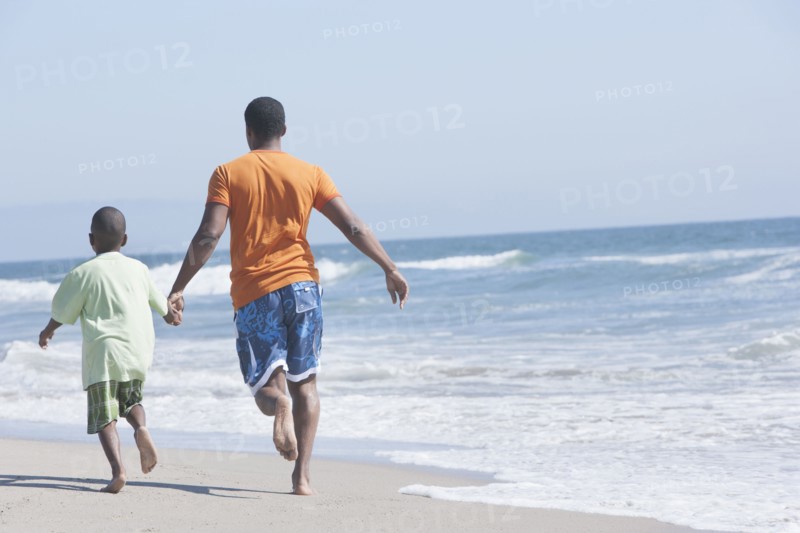 Father and son walking in waves on beach