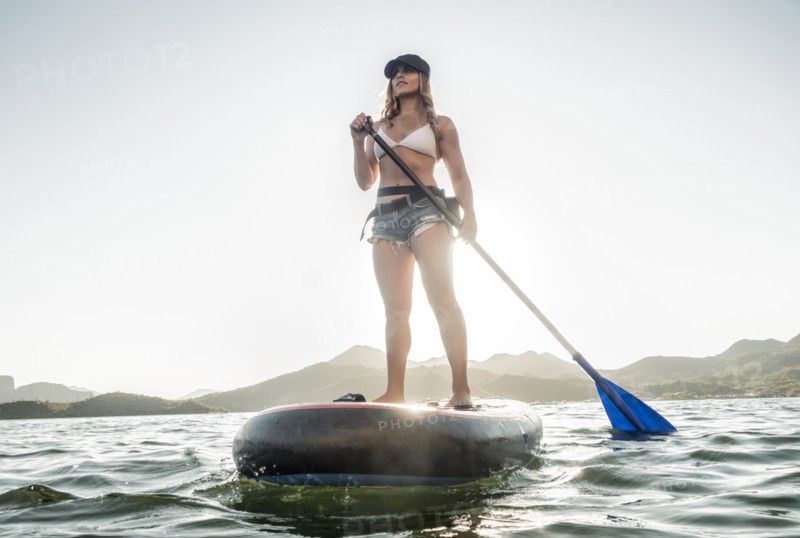 Hispanic woman standing on paddleboard in river