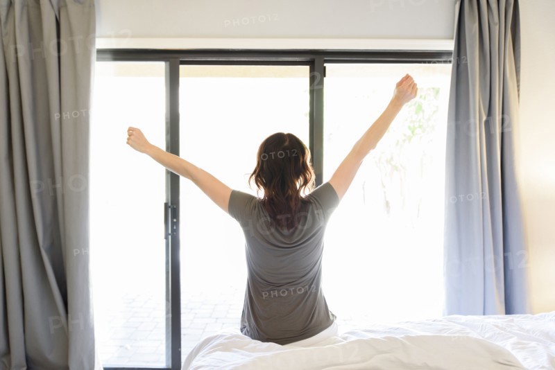 Caucasian woman sitting on bed stretching arms