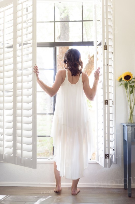 Caucasian woman wearing nightgown opening window shutters