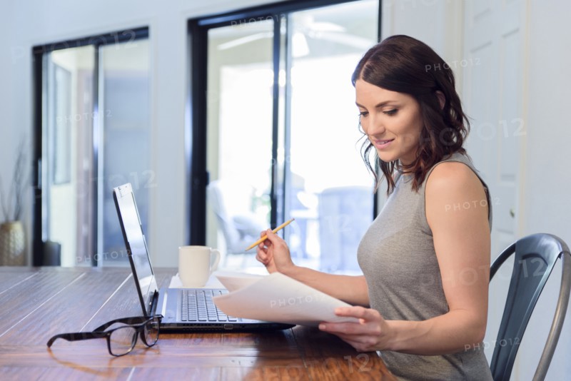 Caucasian woman reading paperwork and using laptop