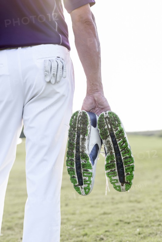 Hispanic man hold golf shoes covered with grass