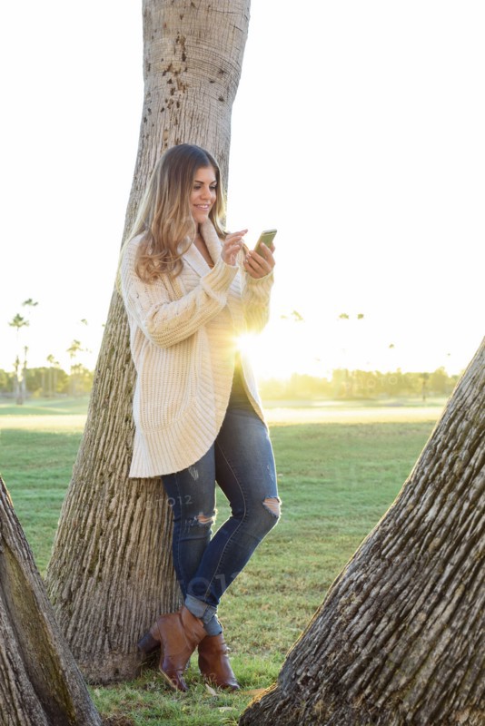 Hispanic woman leaning on tree texting on cell phone