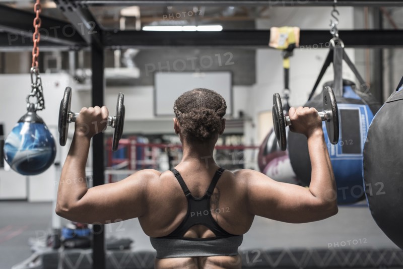 Black woman lifting dumbbells in gymnasium