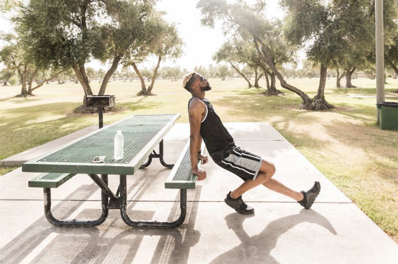 Black man leaning on picnic table in park stretching leg