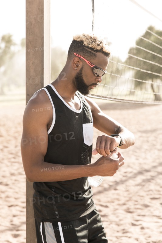 Black man leaning on beach volleyball net checking the time