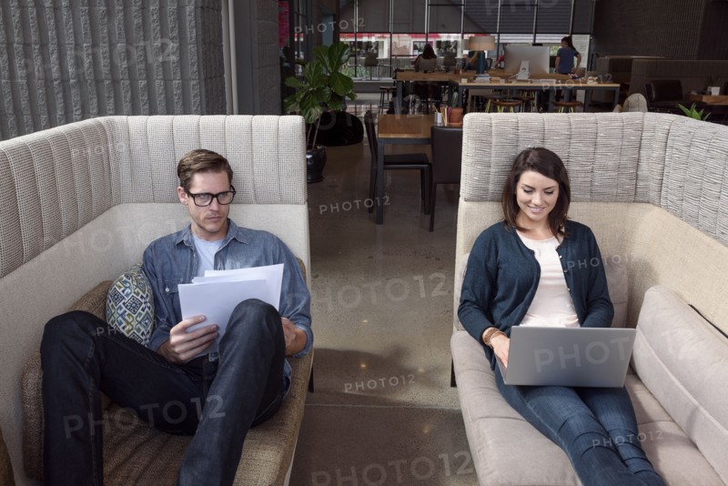 Caucasian couple on sofas using laptop and reading paperwork