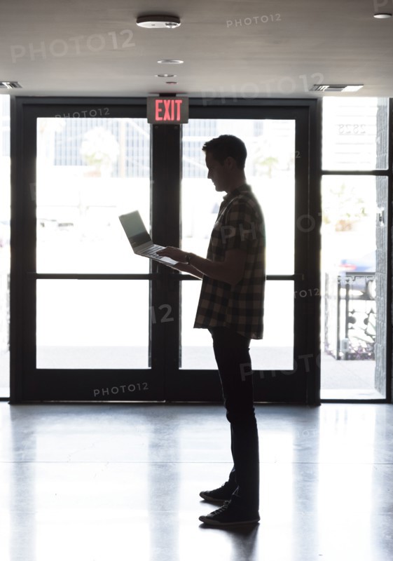 Caucasian man standing near doorway using laptop