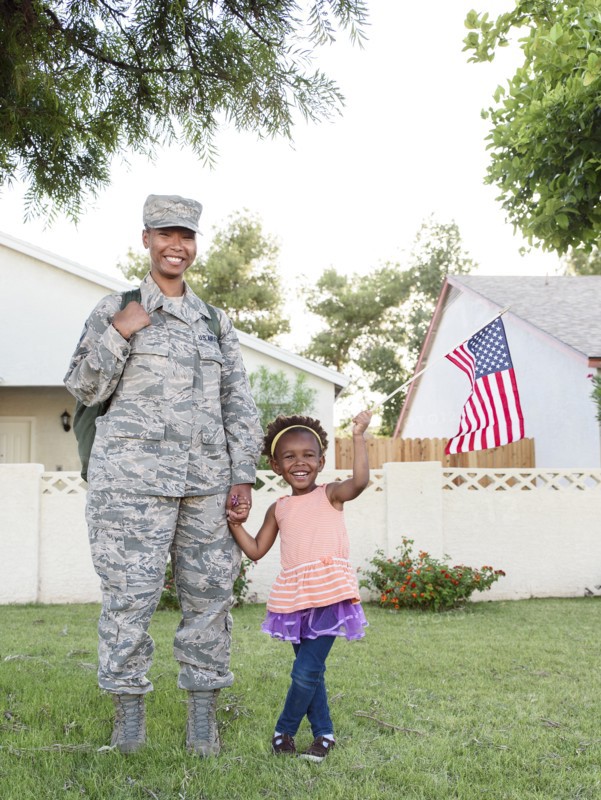 Smiling black woman soldier with daughter waving American flag