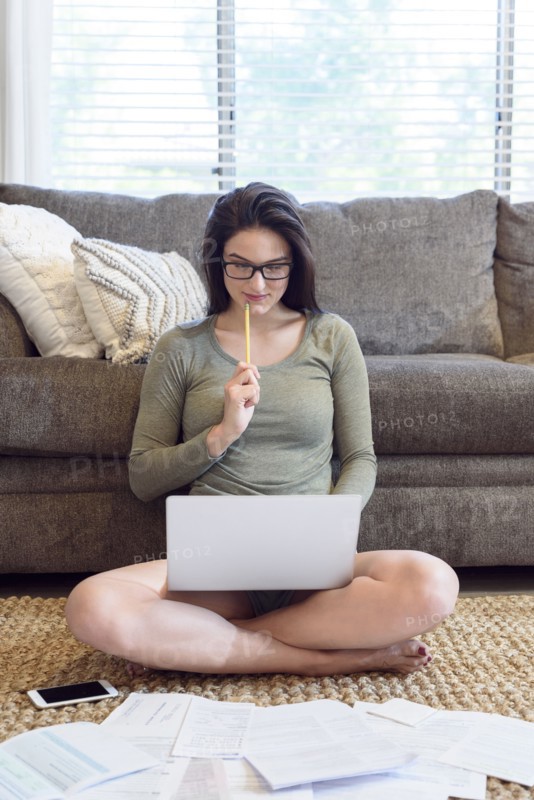 Caucasian woman sitting on floor using laptop near paperwork
