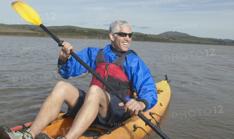 Middle-aged man rowing a kayak in still water