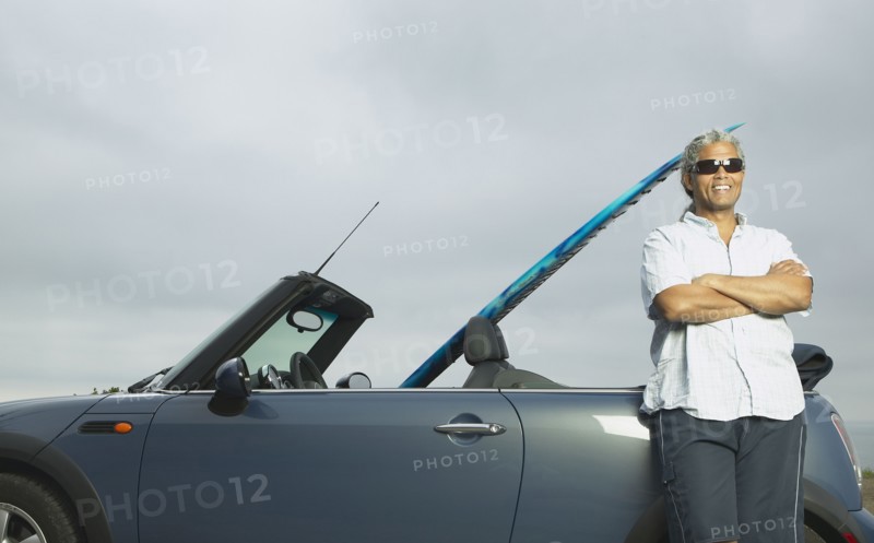 Senior man leaning on a convertible with a surfboard in it