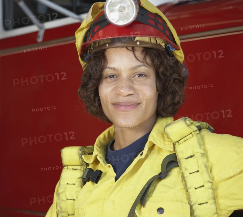 African female firefighter leaning against fire truck