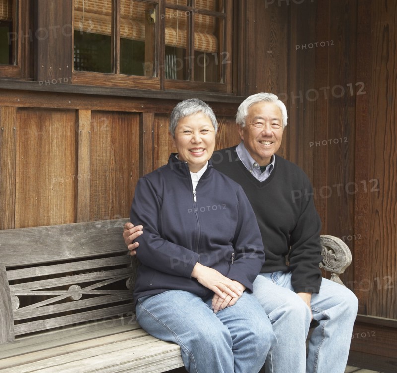 Senior Asian couple smiling and sitting on bench outdoors