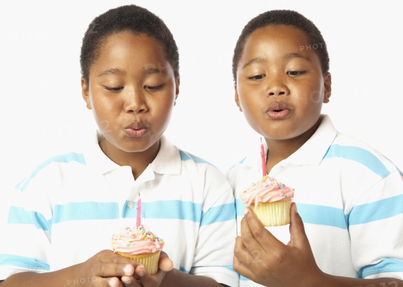 Young African twin brothers holding cupcakes with candles