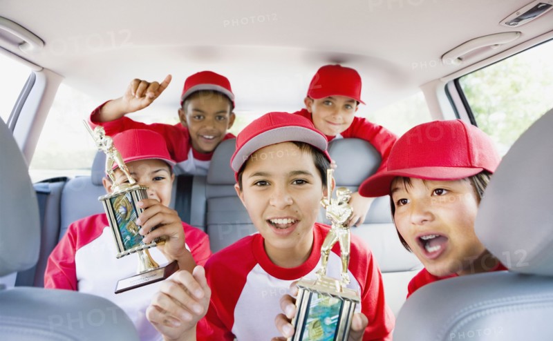 Multi-ethnic boys in car wearing baseball uniforms and holding trophies
